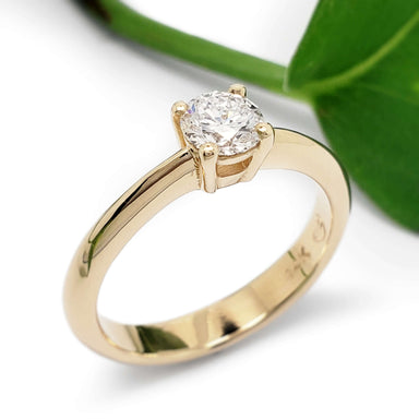 Handcrafted yellow gold solitaire ring with round brilliant diamond, near green leaf