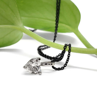 Heart-shaped lab diamond pendant in white gold with black chain, styled on a green leaf