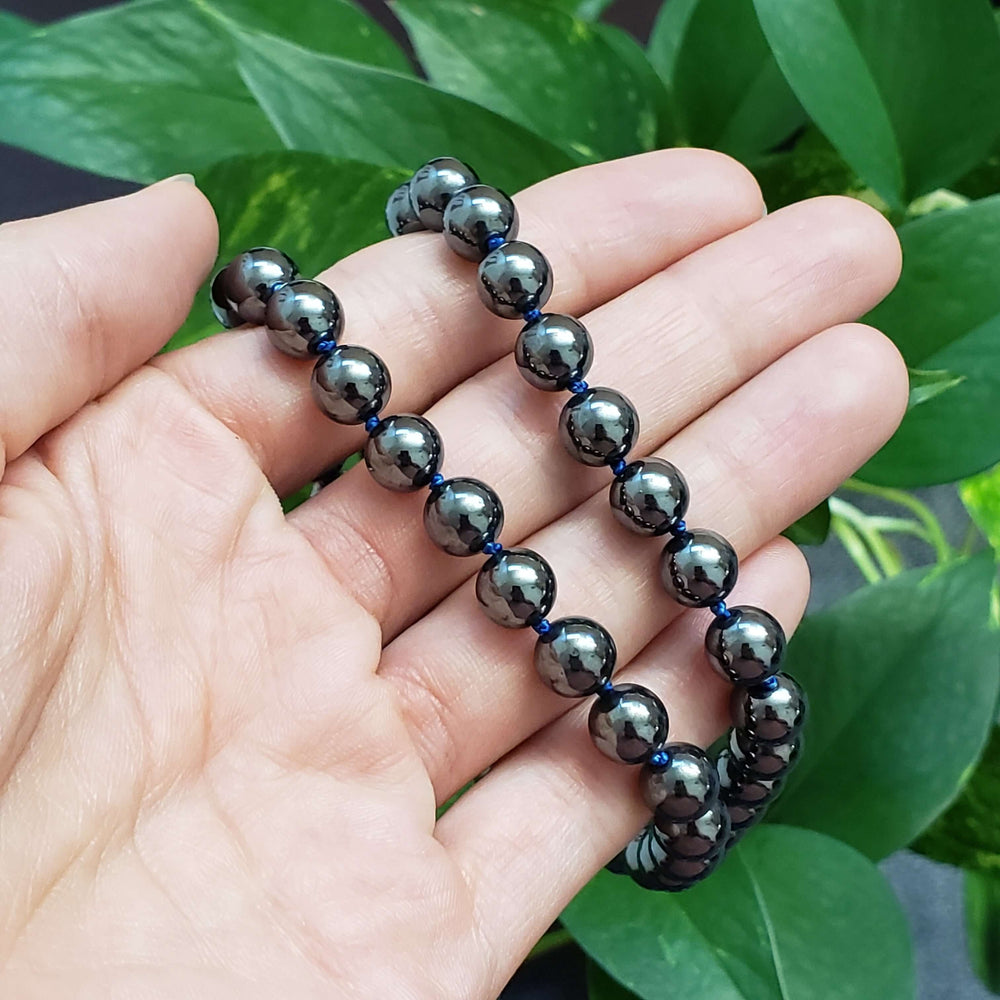 Polished hematite bead necklace displayed in hand with green leaves in background