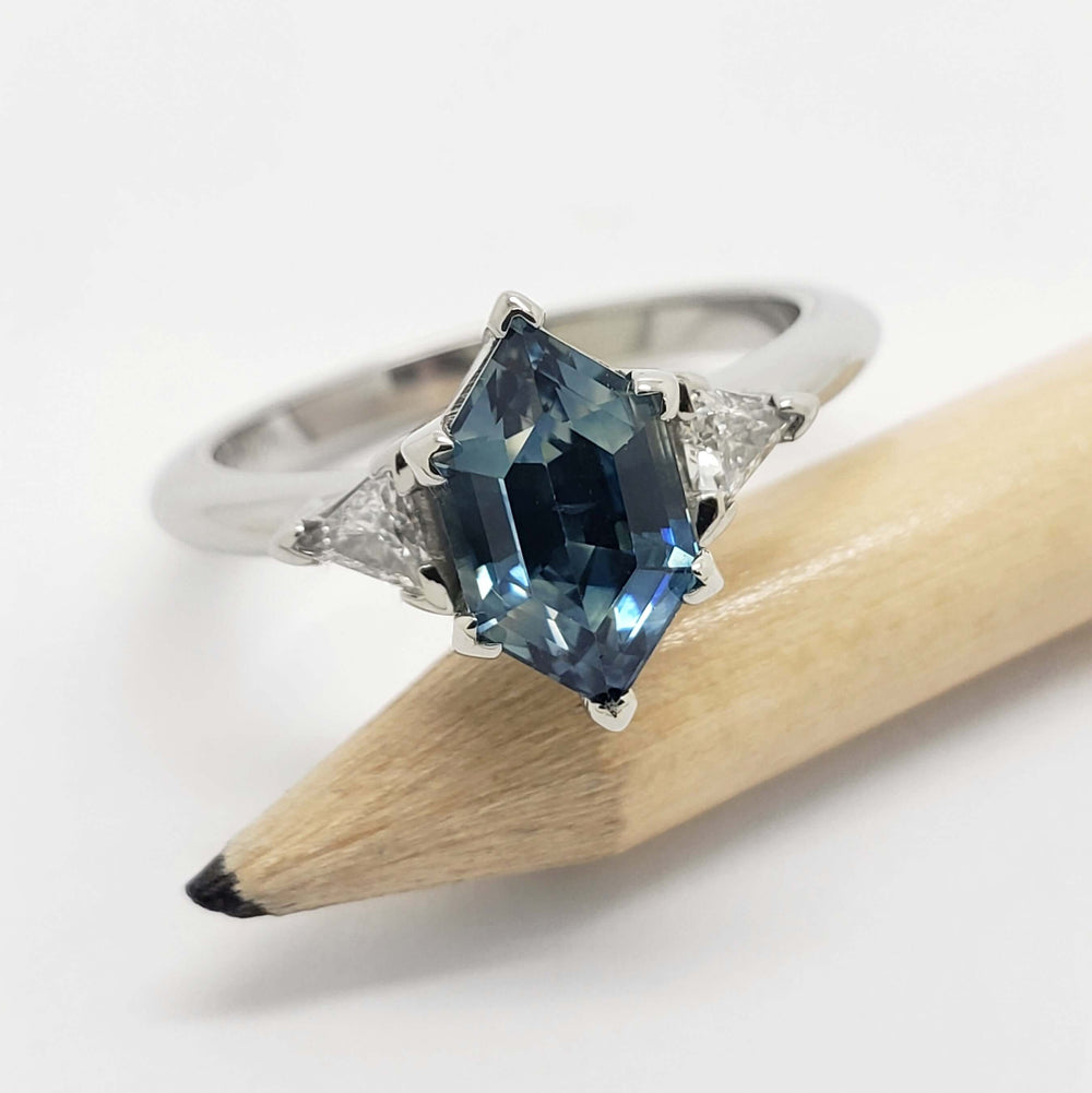 Hexagon blue Montana sapphire and triangle diamond ring in white gold, shown on a pencil
