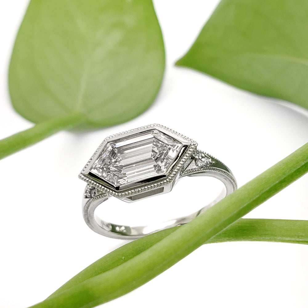 Hexagon lab diamond engagement ring in white gold displayed with green leaves