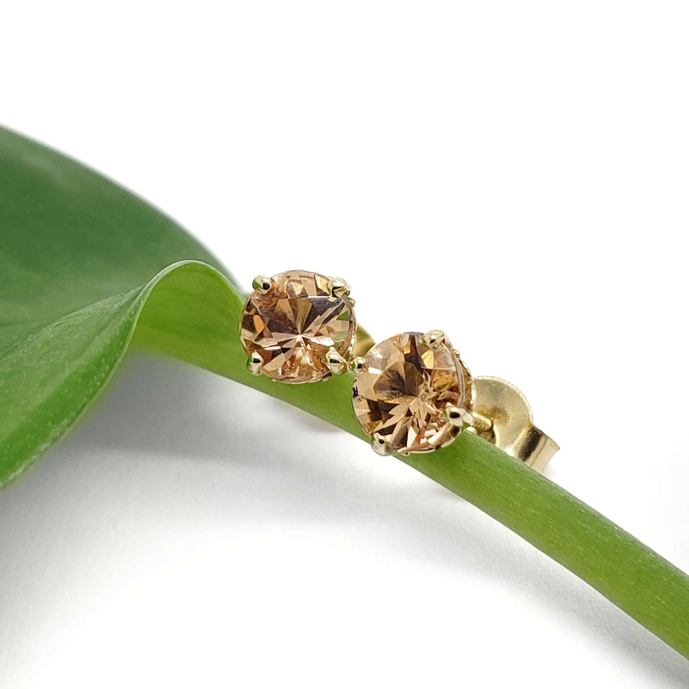 Imperial topaz 14kt yellow gold stud earrings resting on a green leaf