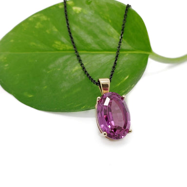 Lab-grown pink sapphire pendant in yellow gold displayed on a green leaf