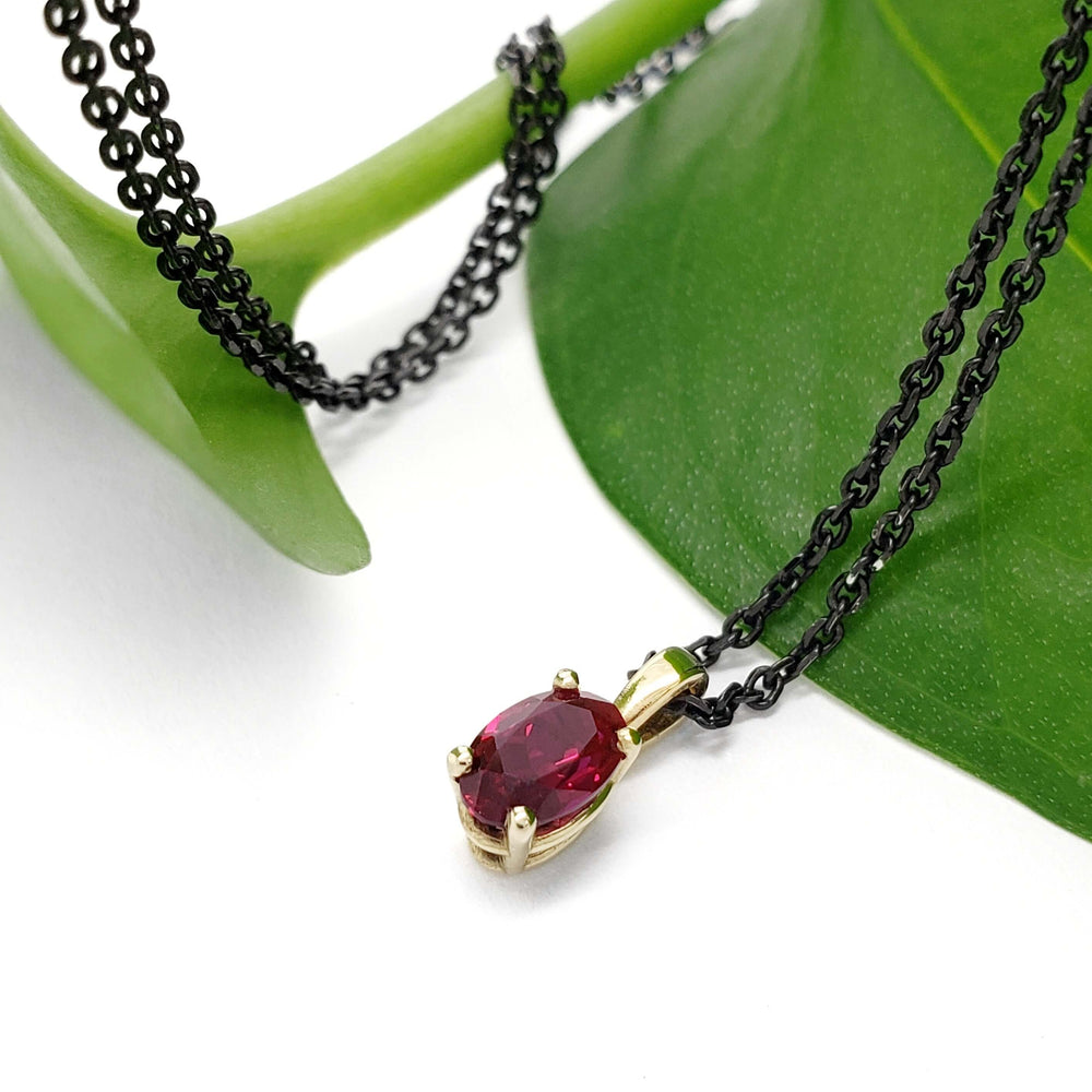Lab-grown ruby pendant in 10kt yellow gold on black chain, styled on a green leaf