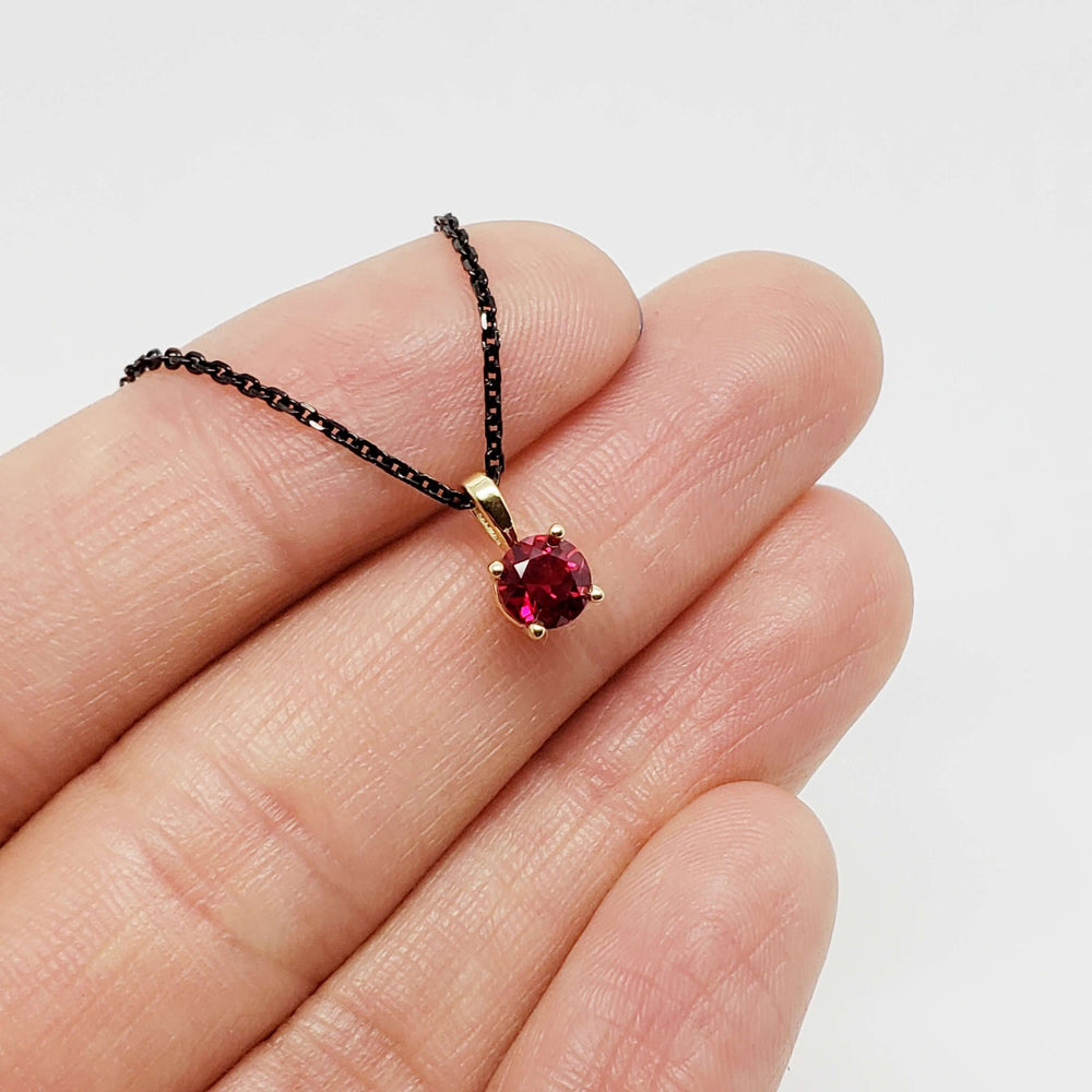 14kt yellow gold lab-grown ruby pendant shown on fingertips for scale