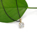 A round-cut clear gemstone pendant on a delicate gold chain, styled on a vibrant green leaf against a clean white background.