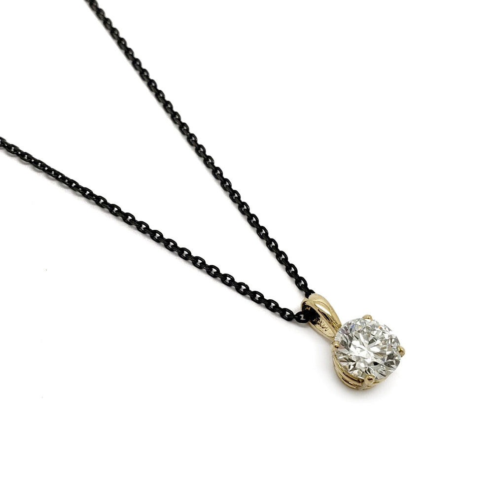 A yellow gold solitaire pendant necklace with a round-cut clear gemstone on a delicate black chain, set against a plain white background.