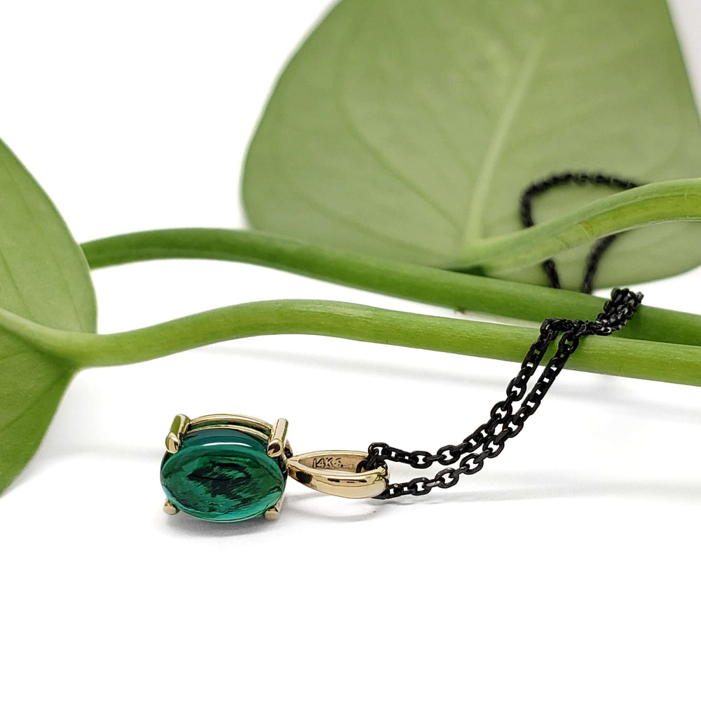 Lab emerald cabochon pendant in 14kt yellow gold with black chain, styled with green leaves