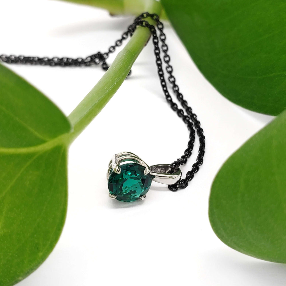 Close-up of lab emerald pendant in 14kt white gold with chain and green leaves