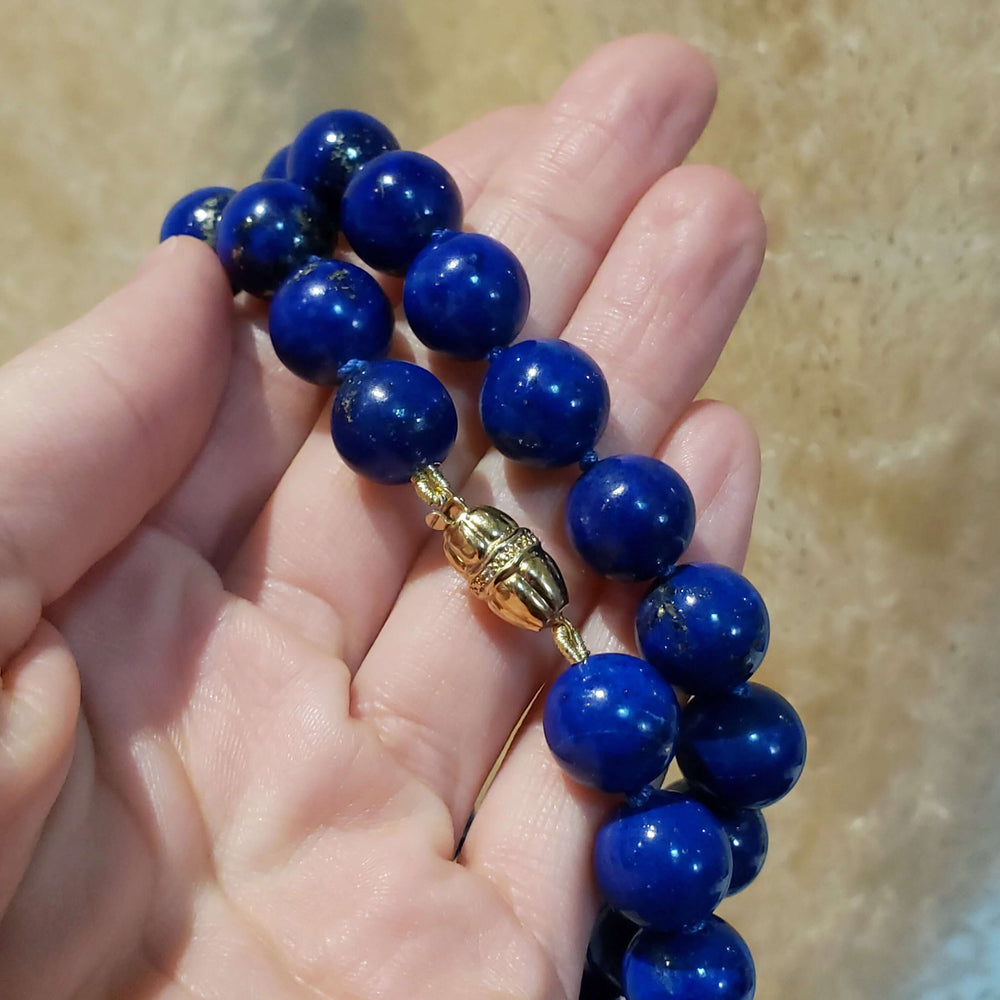 Lapis lazuli bead necklace with gold and diamond clasp shown in hand