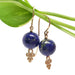 14kt yellow gold lapis lazuli drop earrings with ornate gold details, displayed on a green leaf