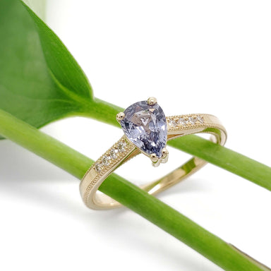 Lavender sapphire and diamond engagement ring in yellow gold resting on a green stem