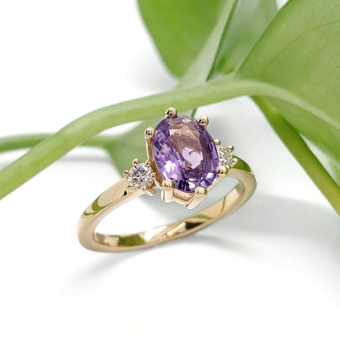 Lavender sapphire and lab diamond engagement ring in yellow gold, displayed with green leaves