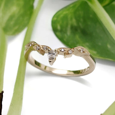 Leaf-inspired 14k yellow gold wedding ring with pear cut diamond, shown with greenery