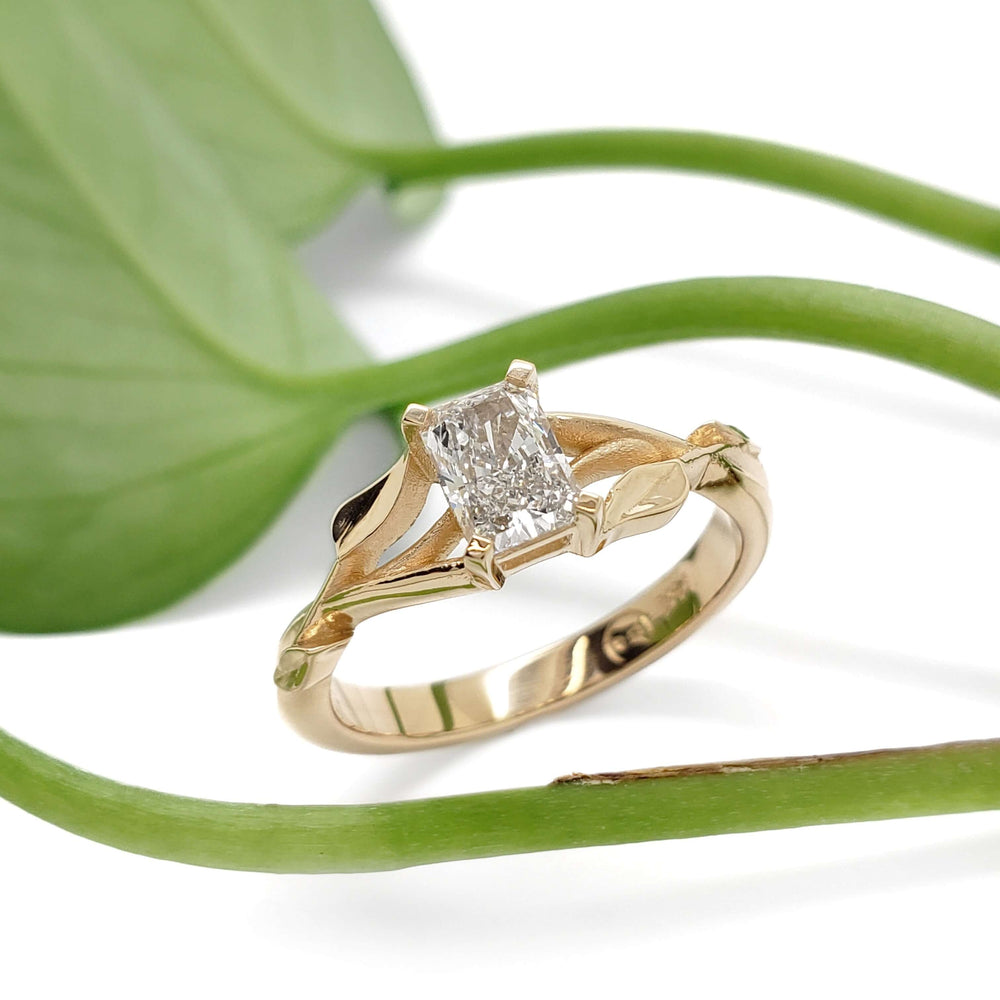 Leaf-inspired 14kt yellow gold lab diamond engagement ring beside green plant
