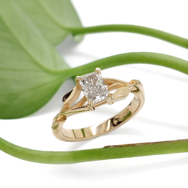 Leaf-inspired 14kt yellow gold lab diamond engagement ring beside green plant