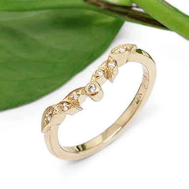 Leaf-inspired yellow gold diamond wedding ring beside a green leaf