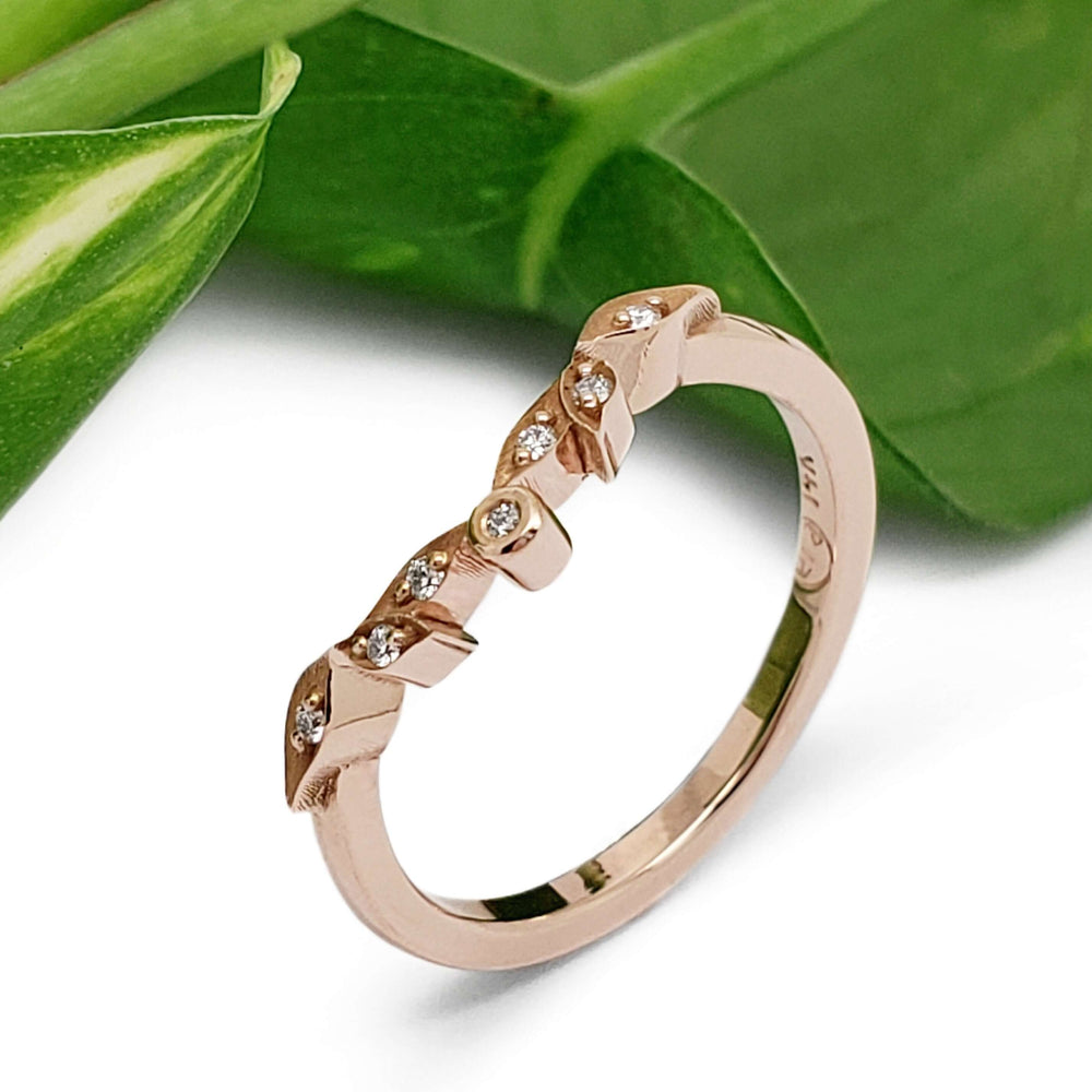 Leafy 14k rose gold diamond wedding ring beside green leaves