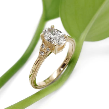 Lucia II 14kt yellow gold lab diamond ring with vintage-inspired accents beside a green leaf