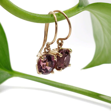 14kt yellow gold drop earrings with oval Madagascar garnets hanging from a green plant stem