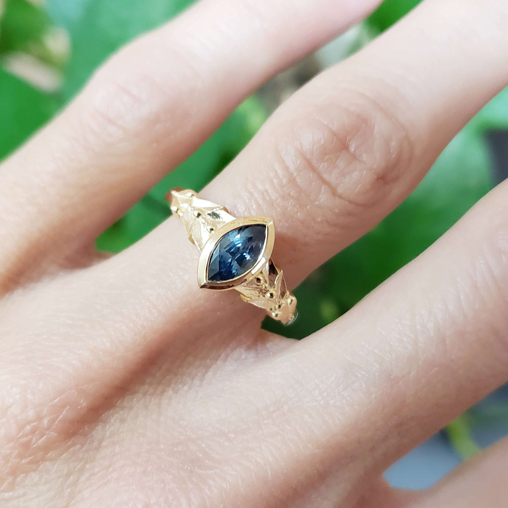 14kt yellow gold marquise Montana sapphire ring worn on hand with leafy background
