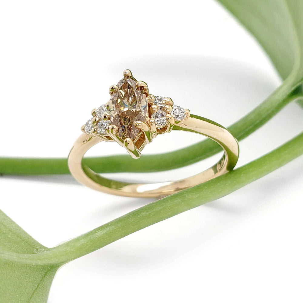 Marquise champagne diamond engagement ring in yellow gold beside green leaves