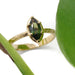 Marquise green sapphire ring in engraved 14kt yellow gold band beside green leaves