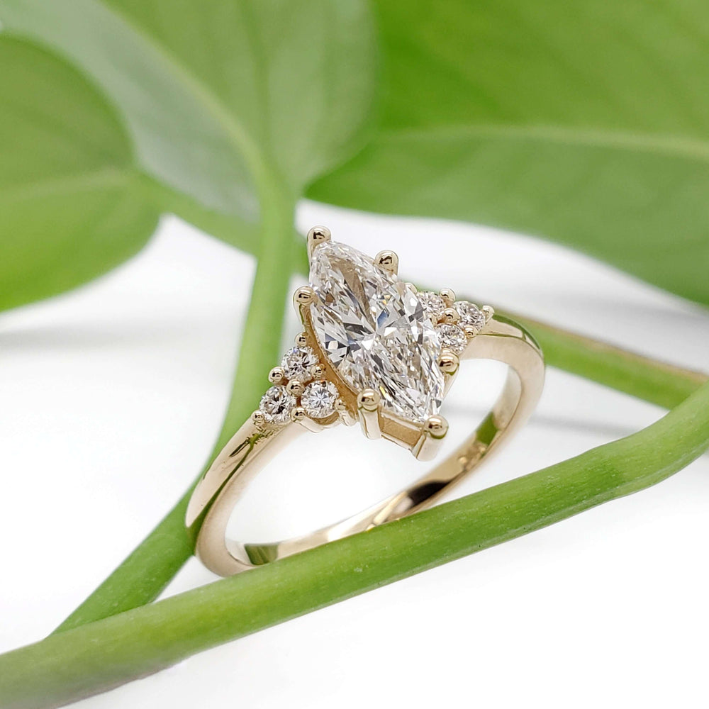 Marquise lab diamond engagement ring in yellow gold resting on green leaves