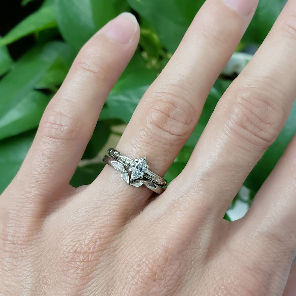 Marquise lab diamond engagement ring with engraved band stacked with leaf band on hand