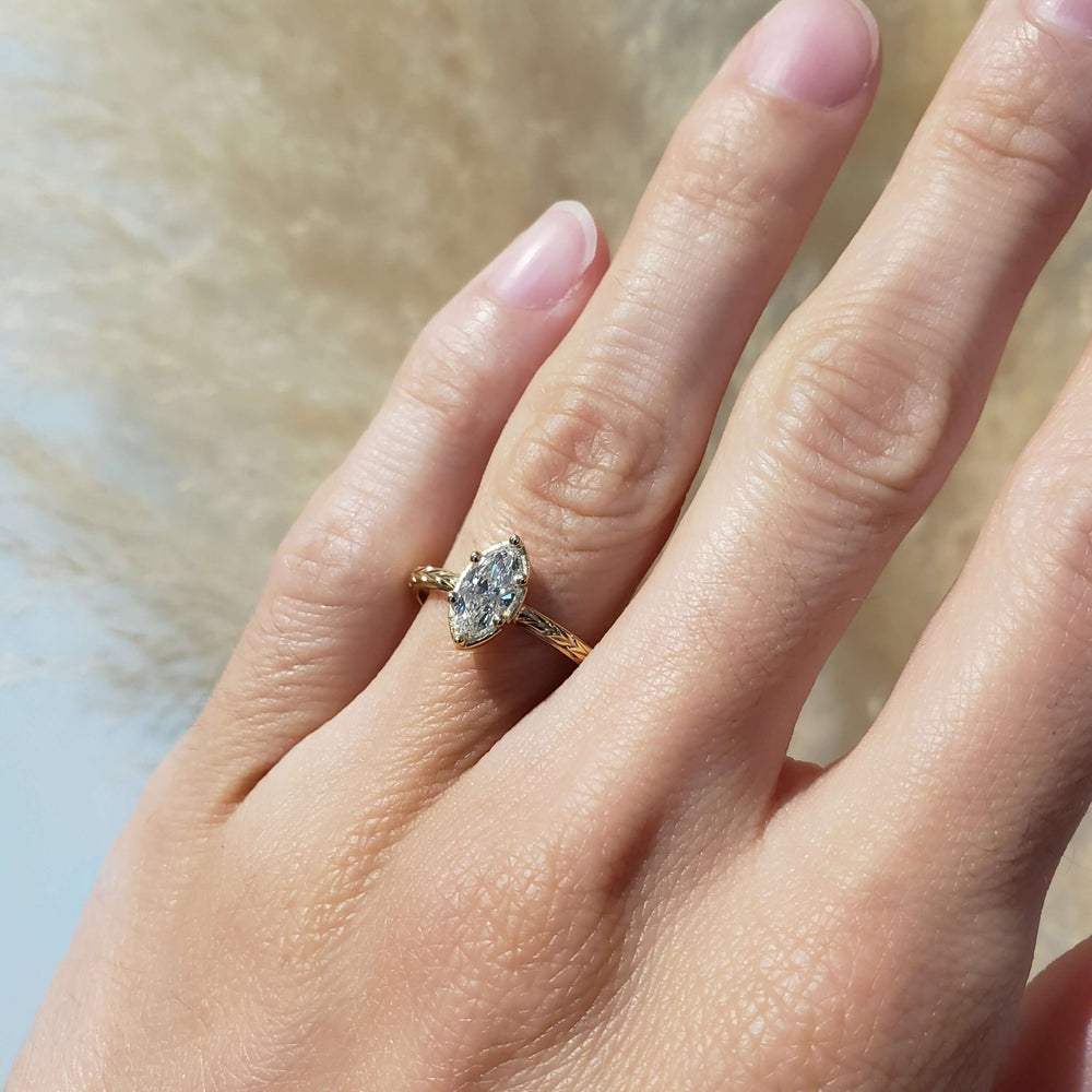 Marquise lab diamond yellow gold engagement ring with engraved band, shown on hand