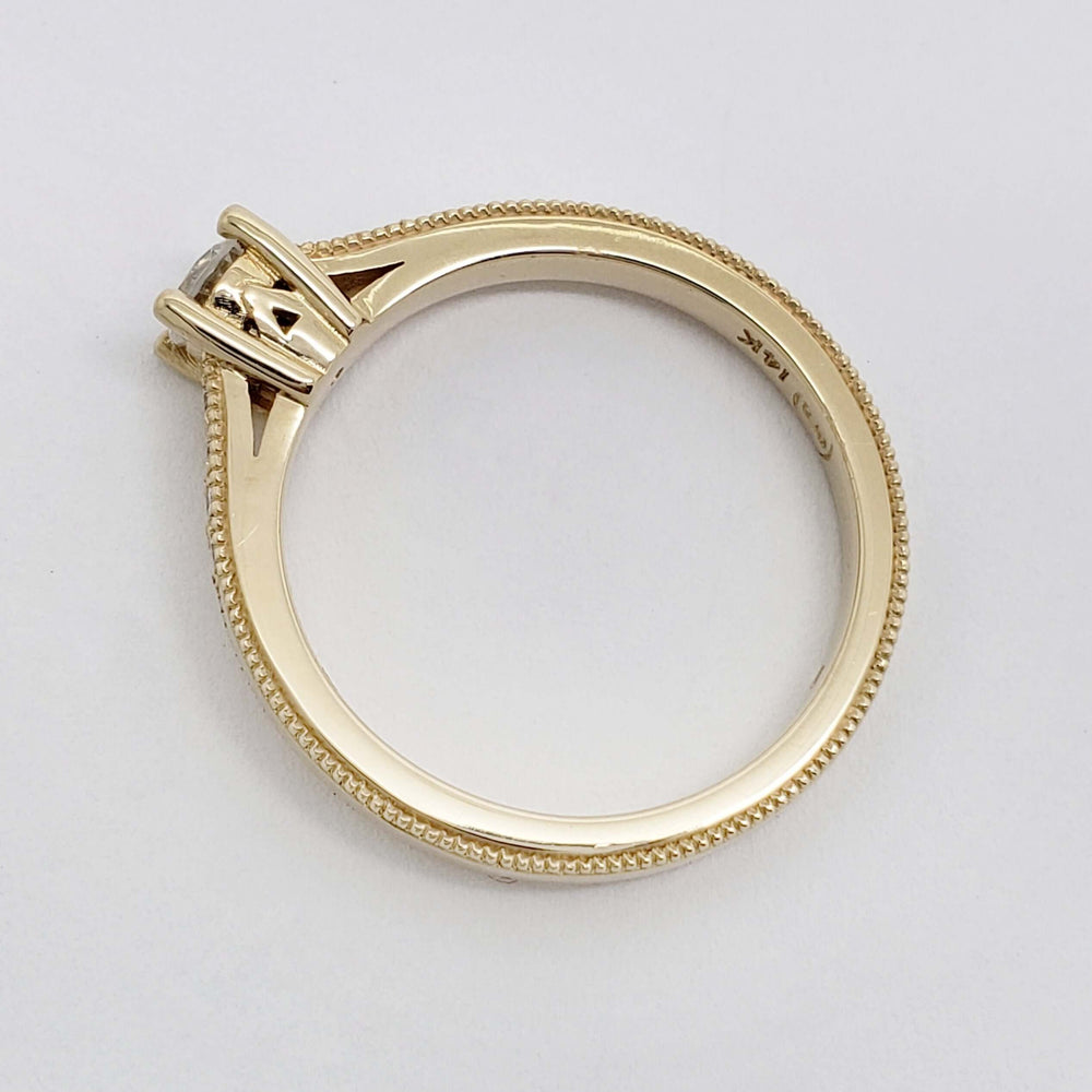 Side view of a yellow gold ring with millgrain edge and raised diamond setting