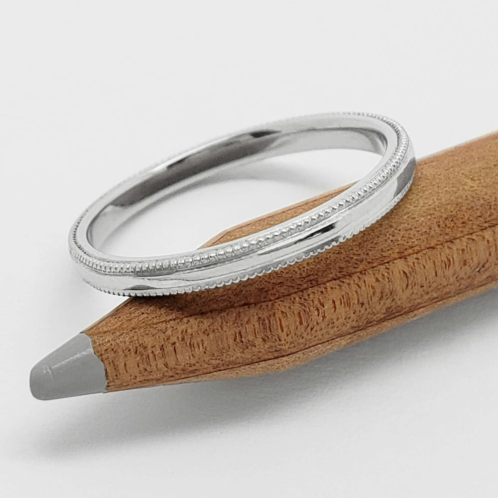 Platinum millgrain wedding band resting on a wooden pencil