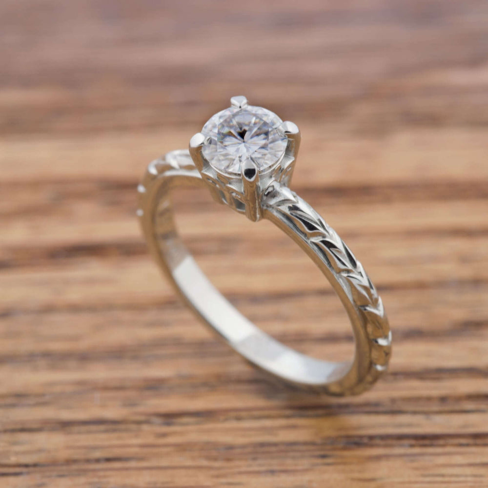 Moissanite engagement ring in white gold with engraved band on wood surface