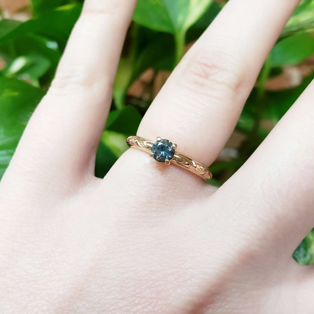 Montana sapphire and 14kt yellow gold engagement ring worn on hand, engraved band visible