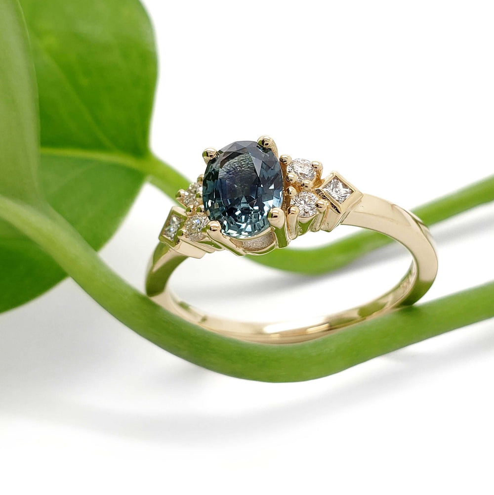 Montana sapphire and diamond engagement ring in 14kt yellow gold beside a green leaf