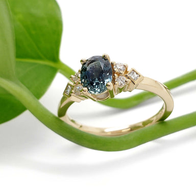 Montana sapphire and diamond engagement ring in 14kt yellow gold beside a green leaf
