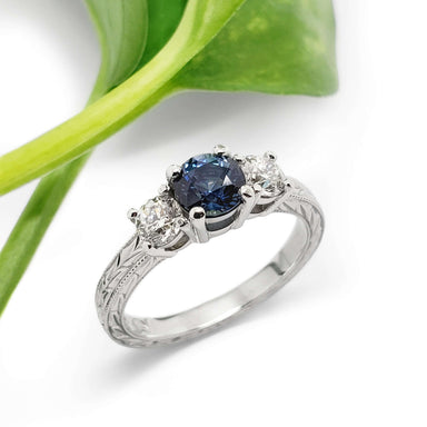 Montana sapphire and diamond engagement ring in white gold with engraved band, beside green leaf