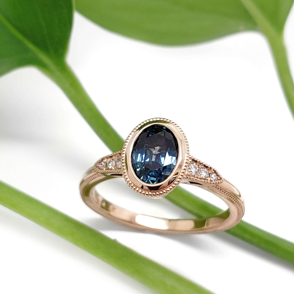 Montana sapphire and diamond engagement ring in 14kt rose gold, shown on white with green leaves