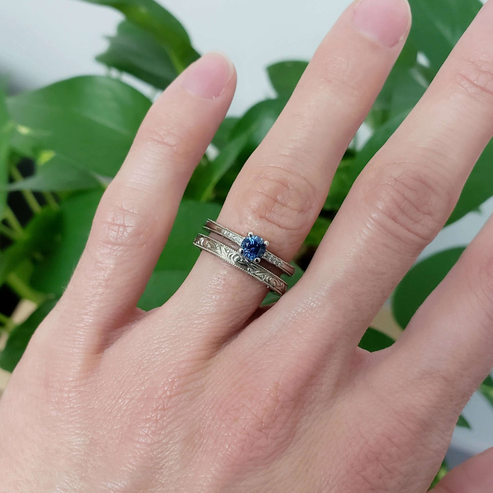 Montana sapphire and diamond ring stacked with two engraved white gold bands, shown on hand