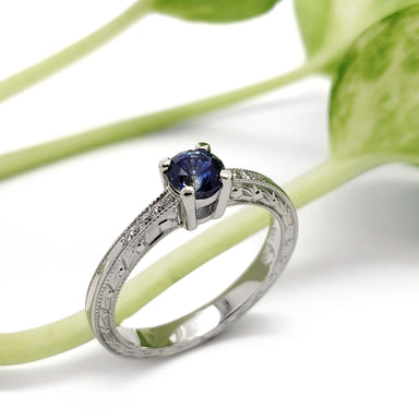 Montana sapphire and diamond engagement ring in white gold with engraved details, beside green plant
