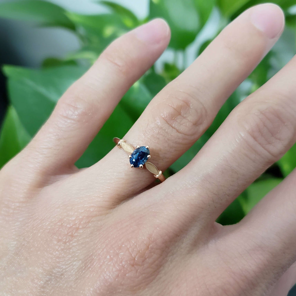 Montana sapphire and rose gold engagement ring on hand, leafy design visible