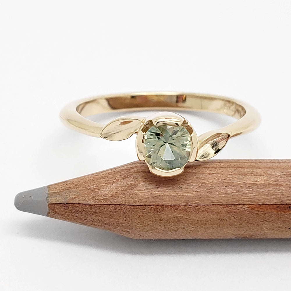 Montana sapphire engagement ring in yellow gold with leaf motif, shown beside pencil