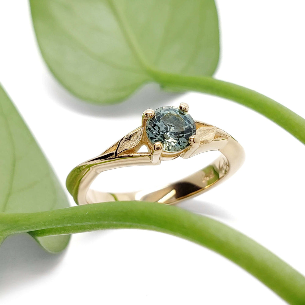 Montana sapphire leaf engagement ring in yellow gold beside green leaves