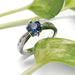 Handcrafted white gold Montana sapphire ring with engraved band, shown with green leaves
