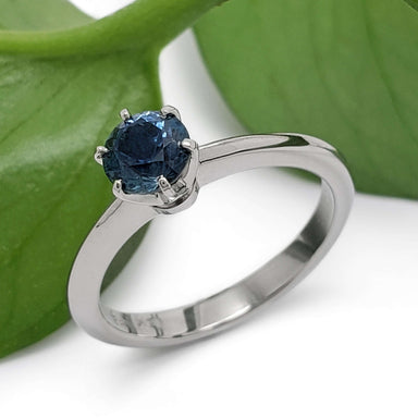 Montana sapphire solitaire engagement ring in white gold beside a green leaf