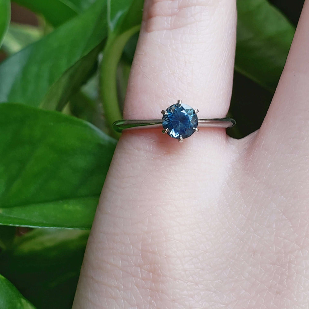 Montana sapphire solitaire ring in white gold shown on a hand with green leaves