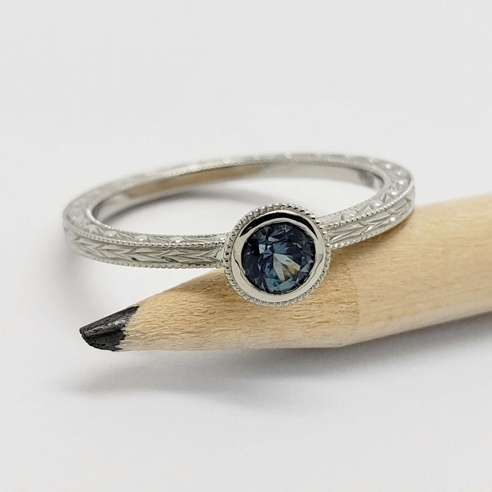 Montana sapphire white gold ring with millgrain bezel, displayed on a pencil