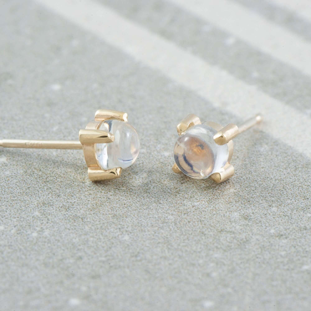 14kt yellow gold moonstone cabochon stud earrings shown on a textured surface