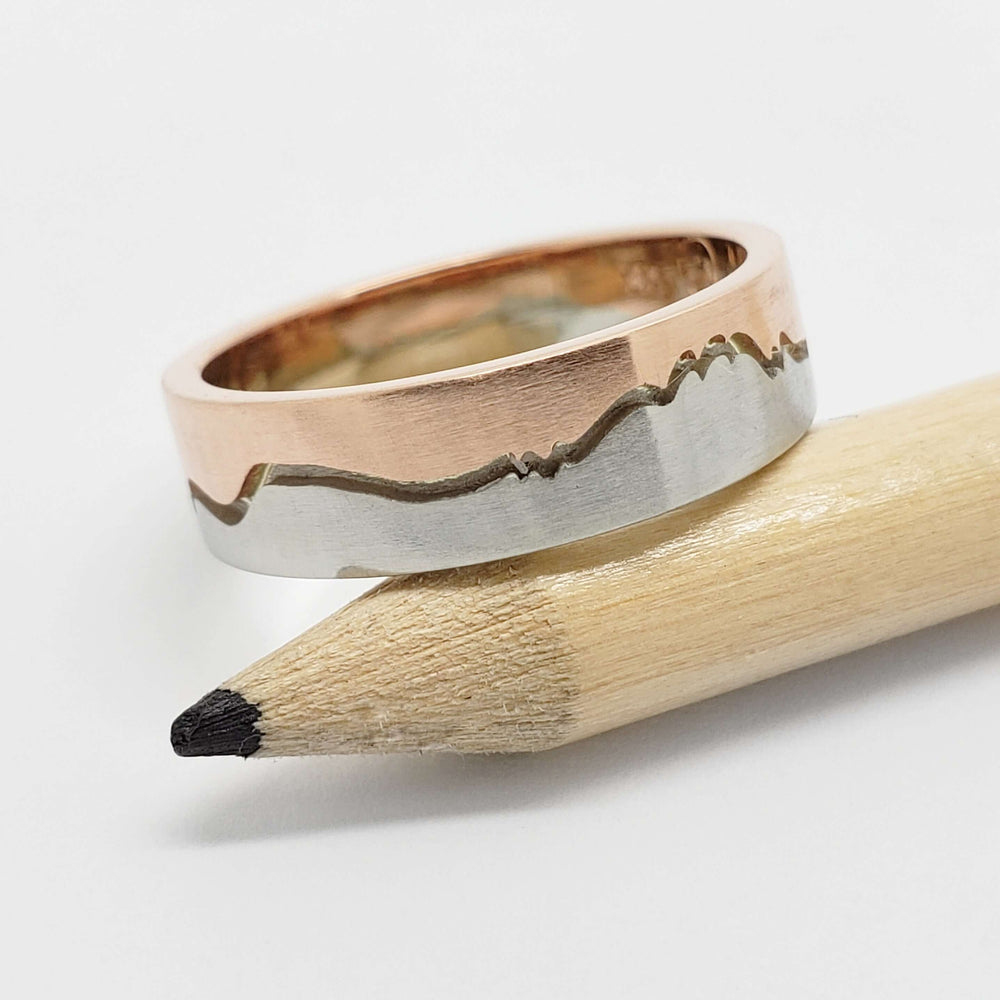 Mountain range wedding band in 14k white and rose gold displayed on a pencil