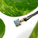 Close-up of 14kt rose gold opal pendant necklace with black chain, surrounded by green leaves